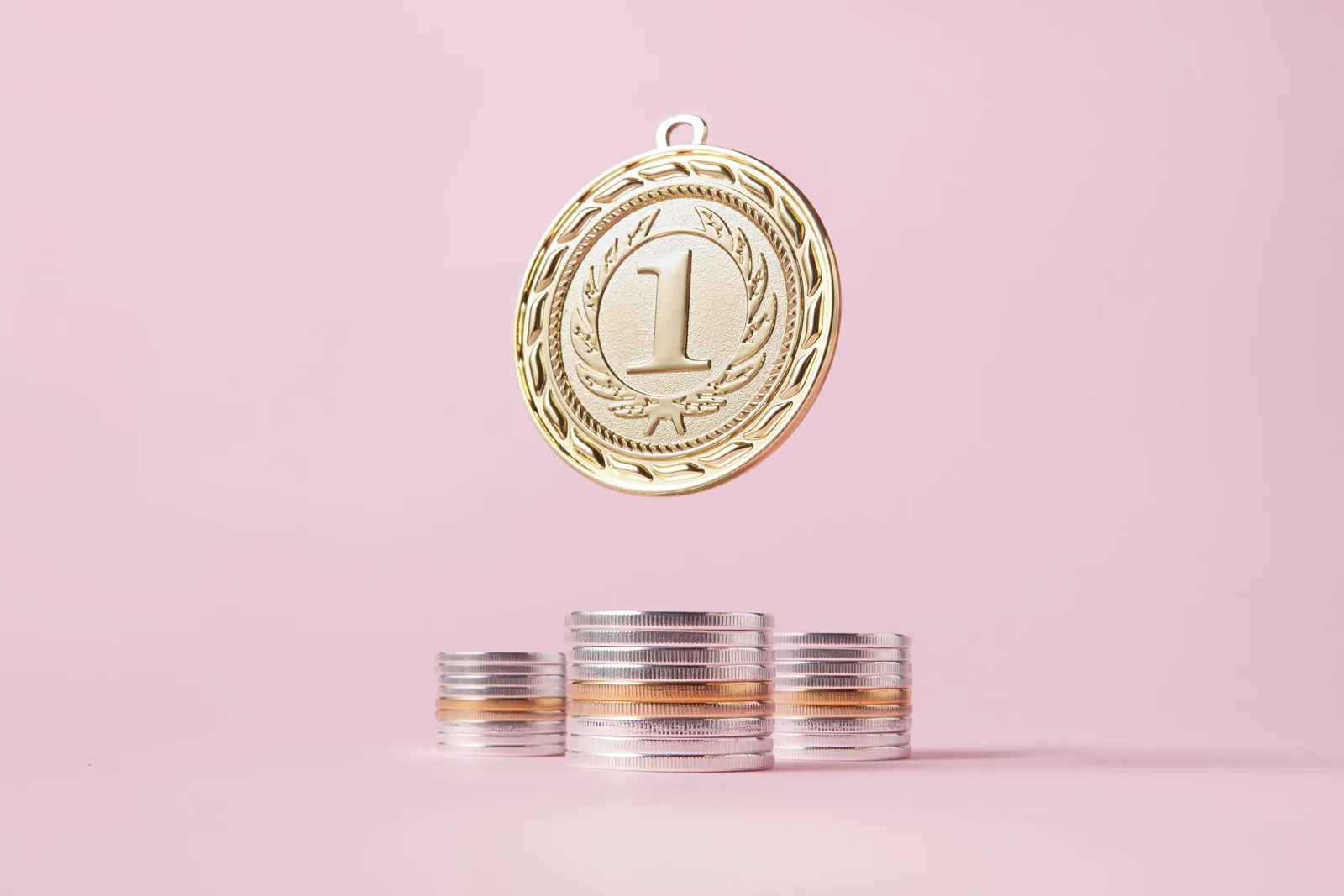 A gold medal and stacks of coins on a light pink backdrop, symbolizing victory and wealth.