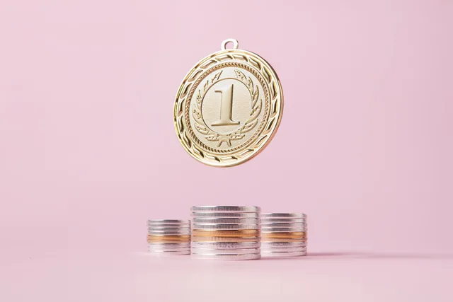A gold medal and stacks of coins on a light pink backdrop, symbolizing victory and wealth. Avoiding rewards that create misleading ad interactions