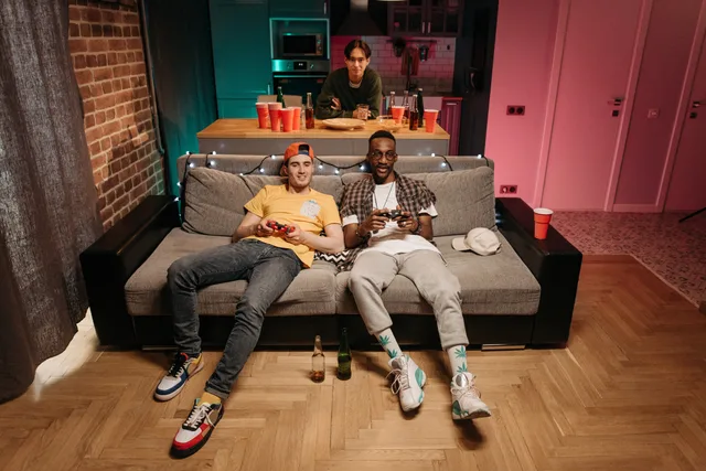 Three friends enjoying a gaming night in a cozy living room with colorful lights and drinks. Gaming audience planning