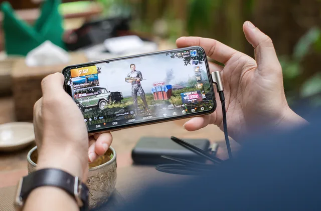 Person playing PUBG on smartphone outdoors with charging cable attached. Reviewing game content before a brand placement