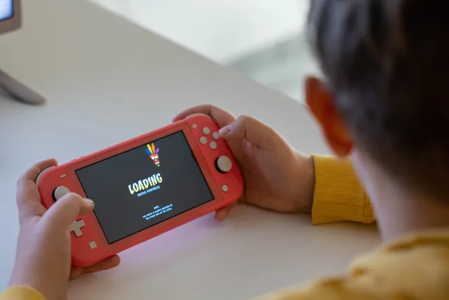 Child holding a pink handheld game console while a digital game loads on the screen. Testing loading time for a playable creative